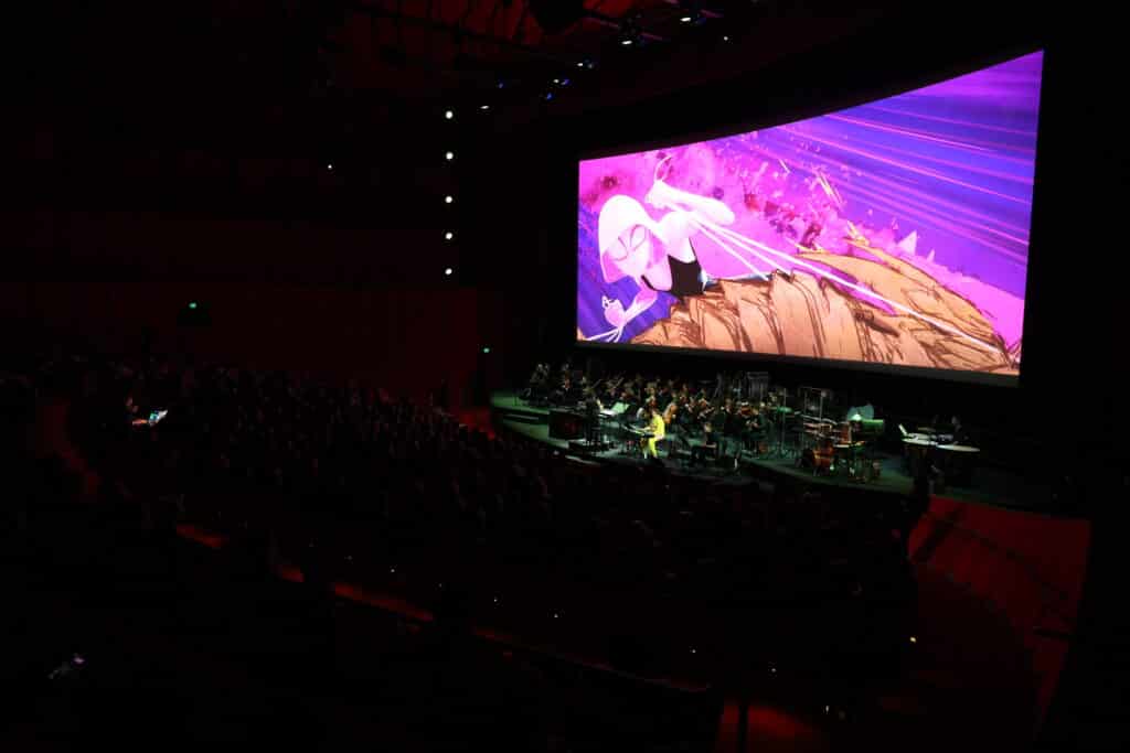 Spiderman in concert being seen above live orchestra on stage.