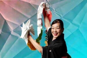 Origami Tales show artwork. Photo shows a woman holding an origami dragon in front of a colorful paper-like background.