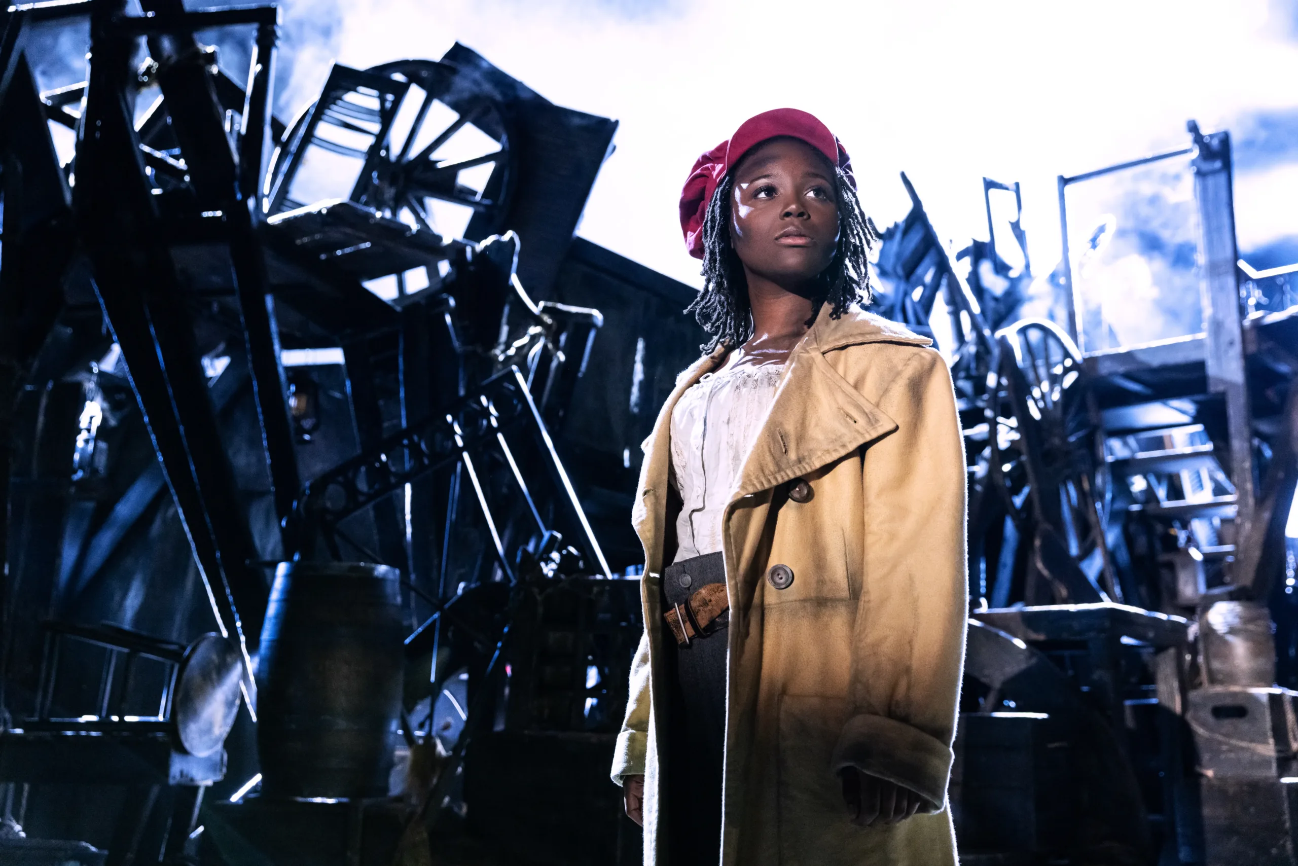 actress in grungy clothing standing in front of a large pile of rubble