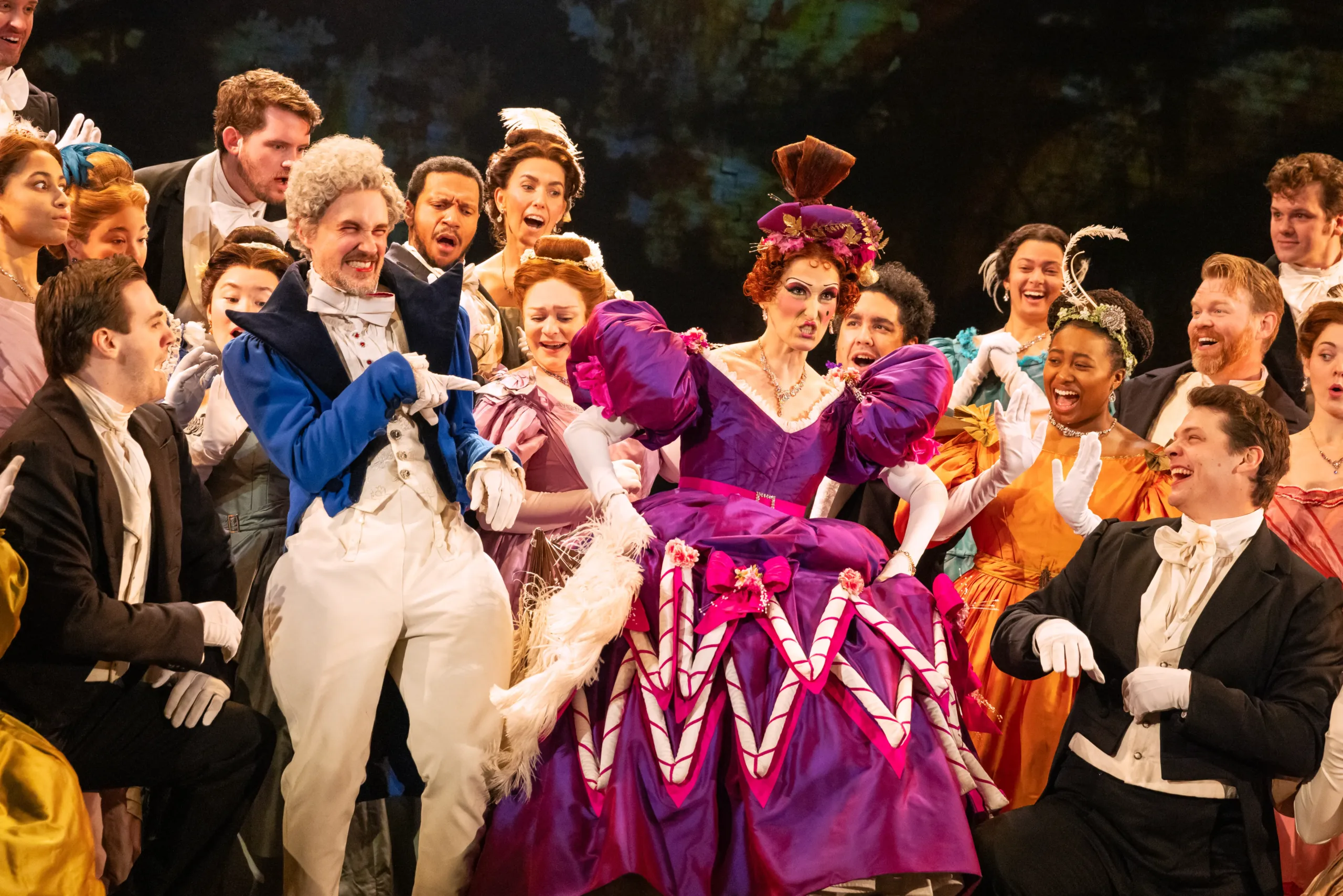 many actors standing around an actress in a pink dress laughing at her