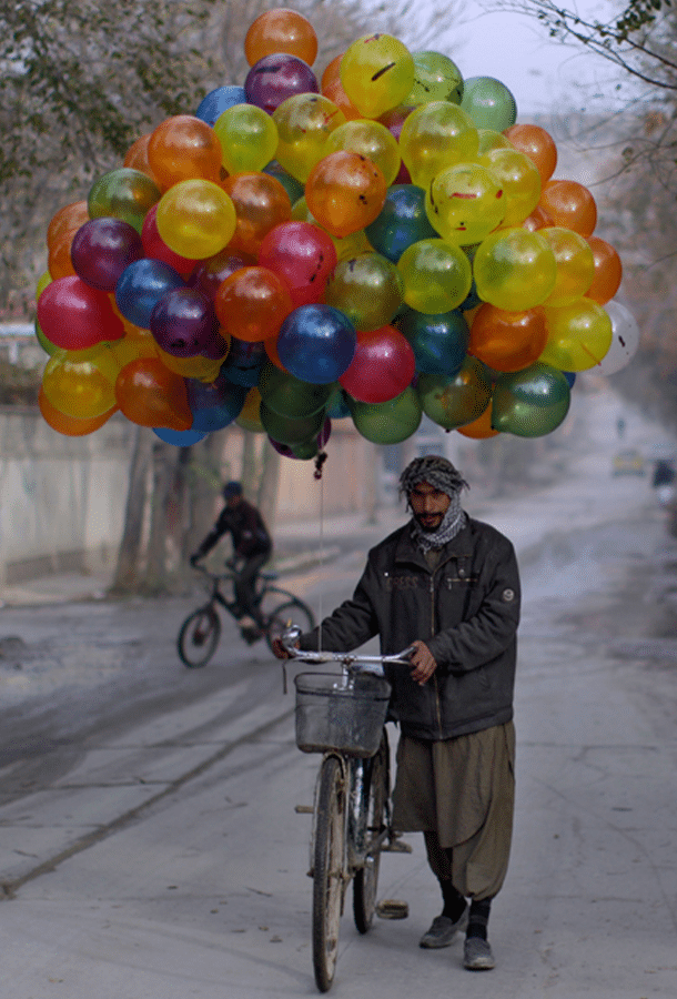 man walking bike with a bouquet of colorful balloons