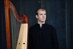 Man (Parker Ramsay) standing beside a harp