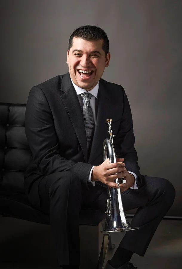 Pacho Flores smiling, seated holding trumpet.