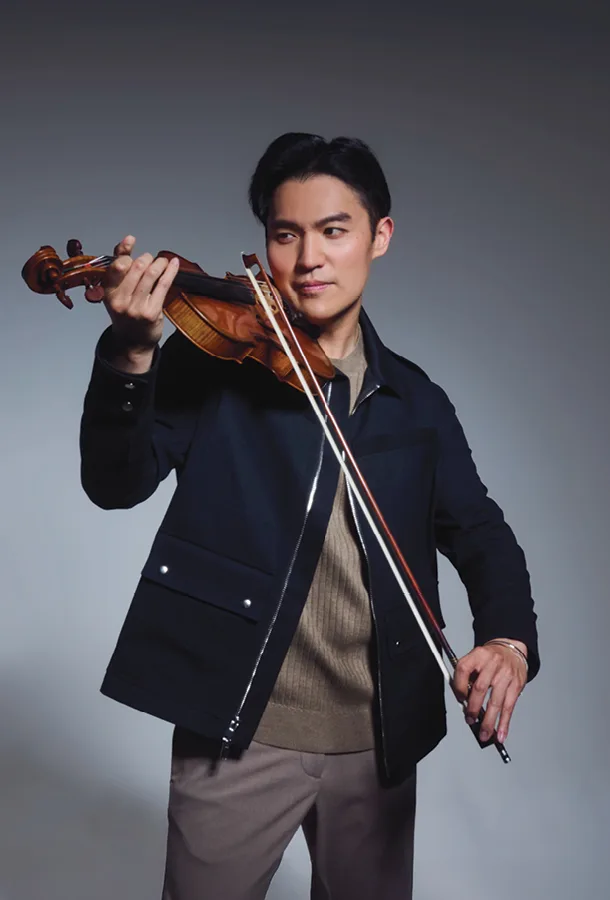 Ray Chen posing with his violin wearing blue jacket.