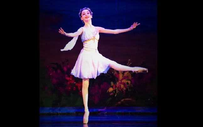 Ballerina in white costume with leg and arms extended. 